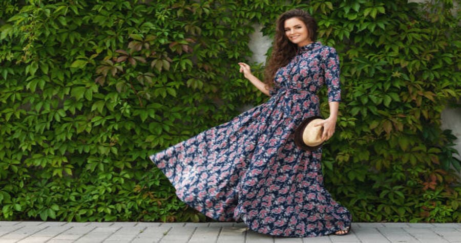 O que a Bíblia ensina sobre Roupas. Uma mulher elegante usando um vestido xadrez, posando ao lado de um muro coberto por plantas verdes.